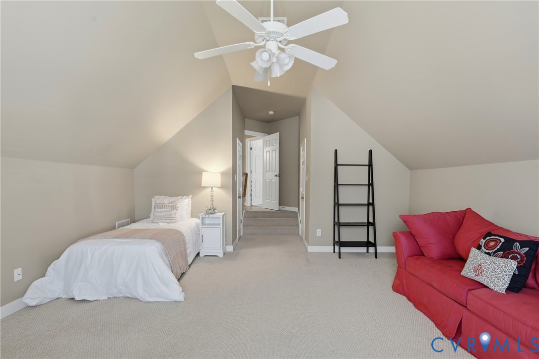 Vaulted ceiling featuring a white multi-blade ceiling fan with integrated lighting and wall-to-wall carpeting