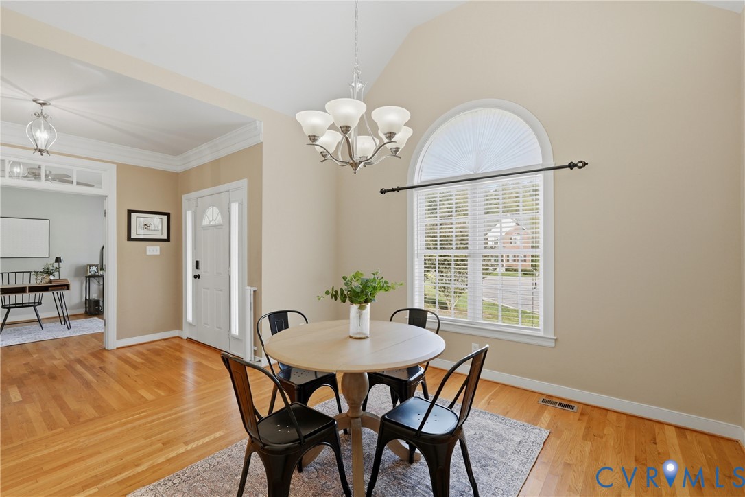Vaulted ceilings, wood-finish flooring, an arched window, and a multi-arm chandelier
