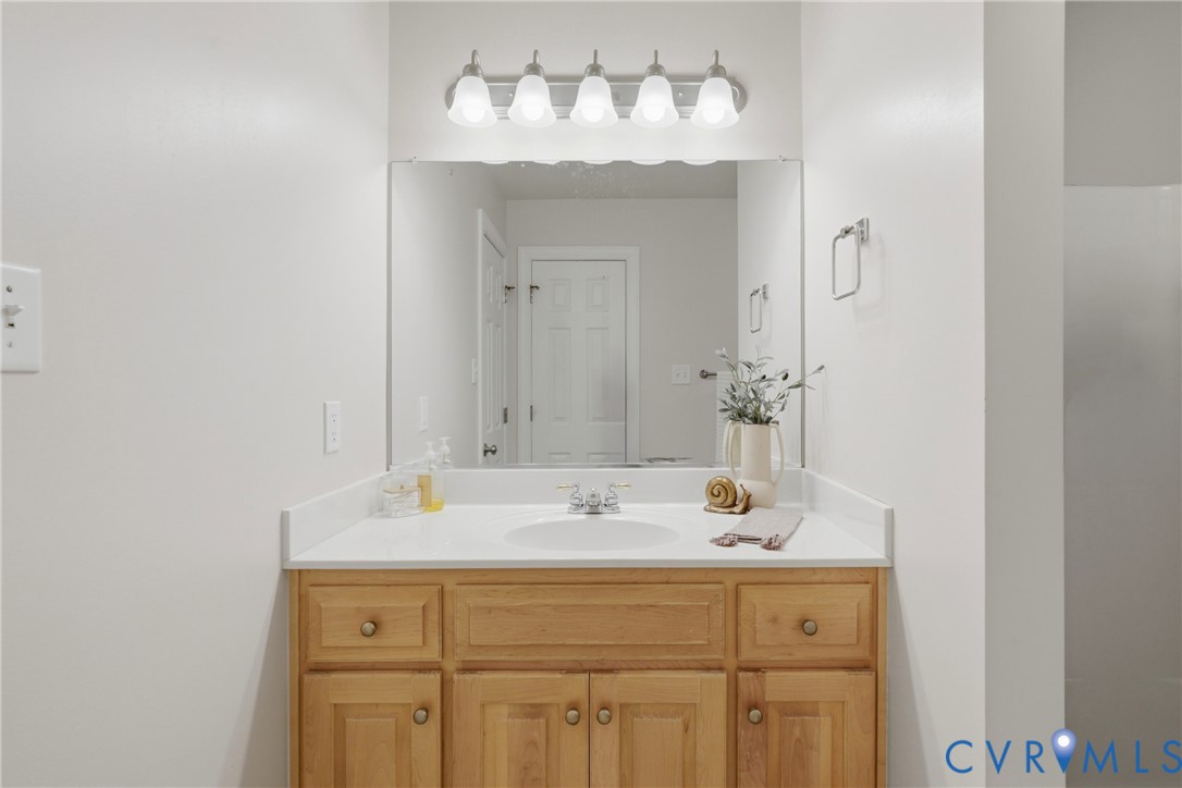 Single-basin vanity with a solid-surface countertop, natural wood cabinetry, large wall-mounted mirror, and five-light vanity fixture