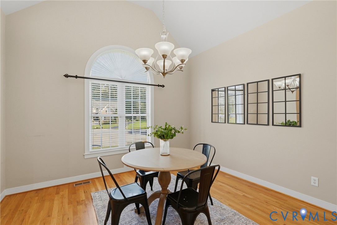 Vaulted ceilings featuring an arched window, wood-finish flooring, and a multi-arm chandelier
