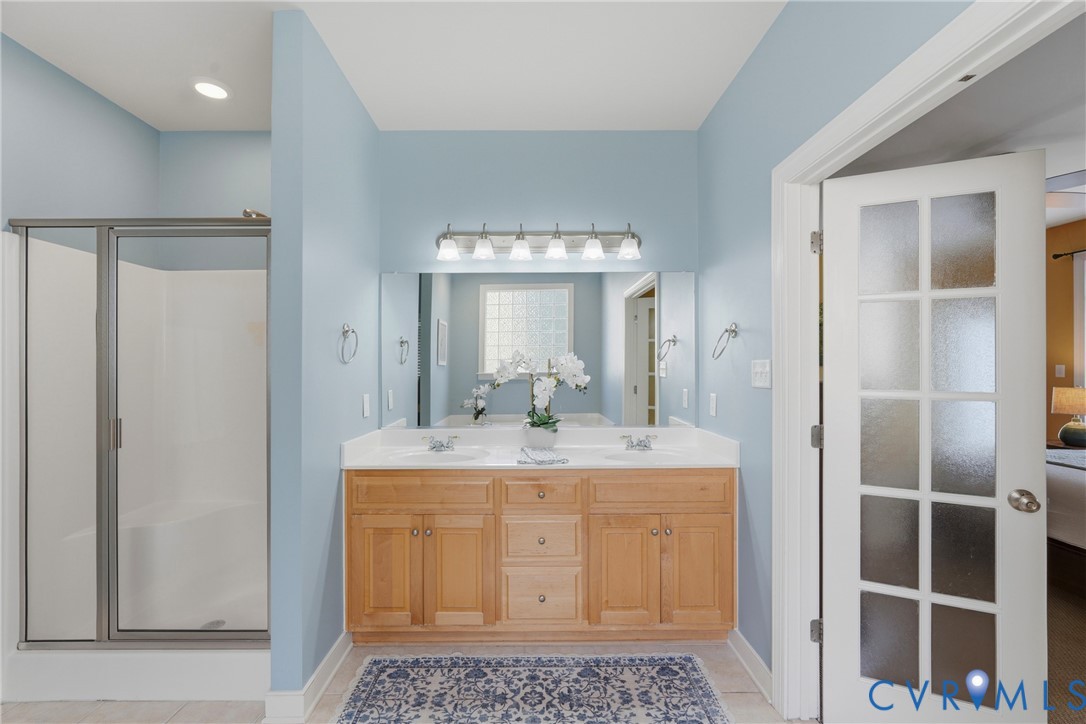 Double vanity with light wood cabinetry, white countertops, recessed lighting, and a glass-enclosed shower