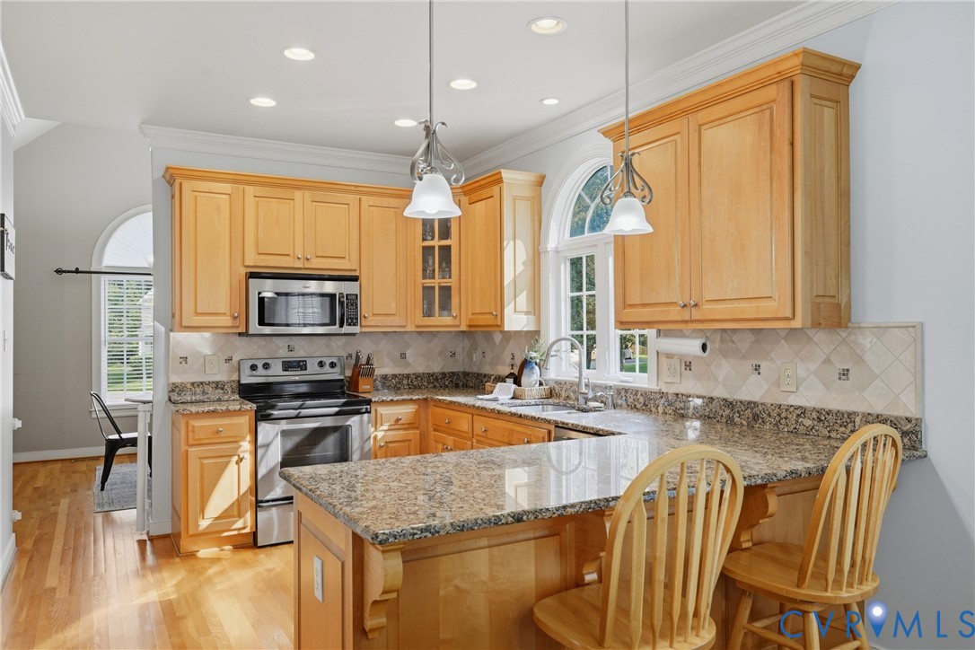 Kitchen featuring wood cabinetry, stone countertops, a tile backsplash, stainless steel appliances, and arched windows