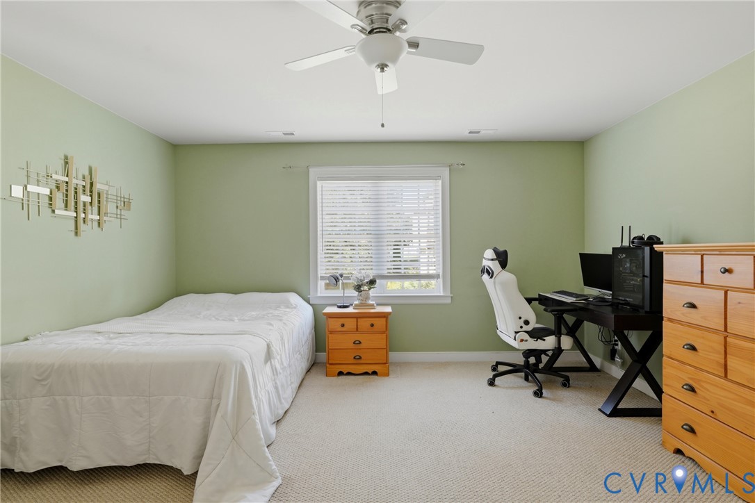Room featuring neutral-toned carpeting, a center-mounted ceiling fan with light fixture, and a central window with slatted blinds