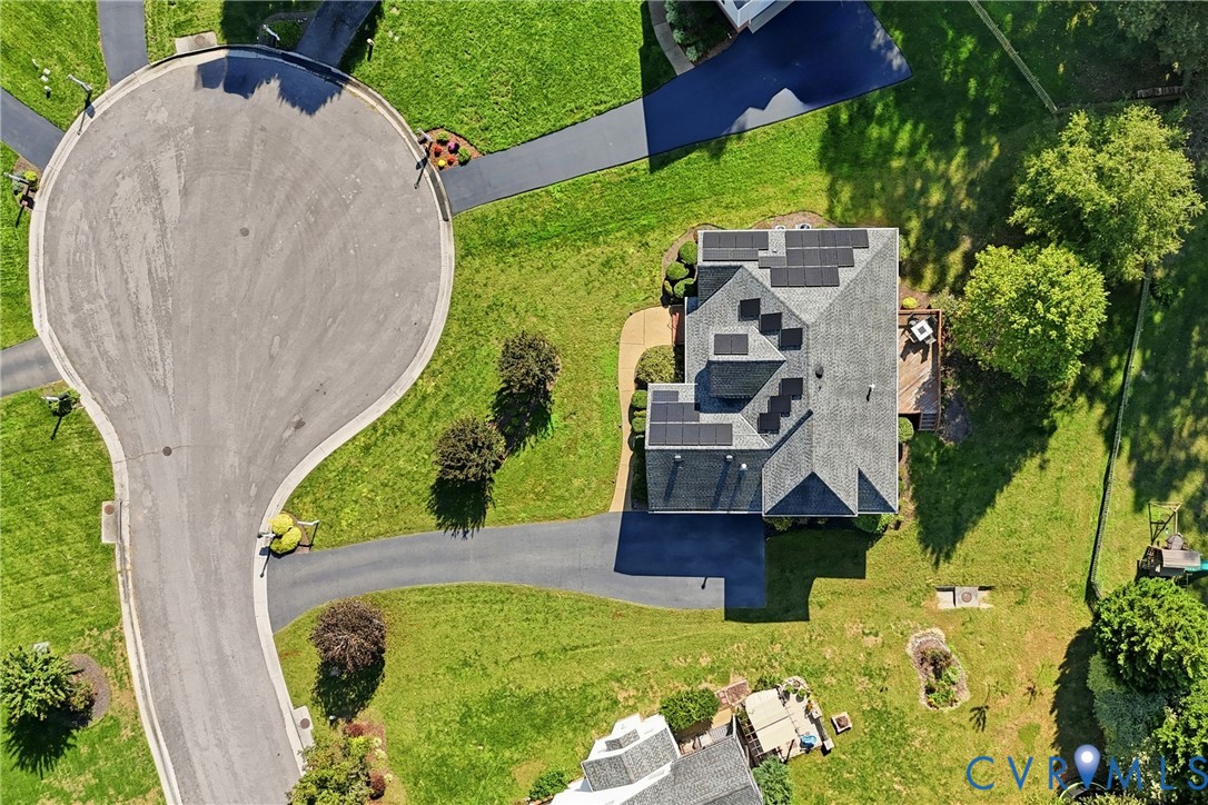 Aerial view of property featuring a shingled roof with integrated solar panels, asphalt driveway, and expansive lawn area