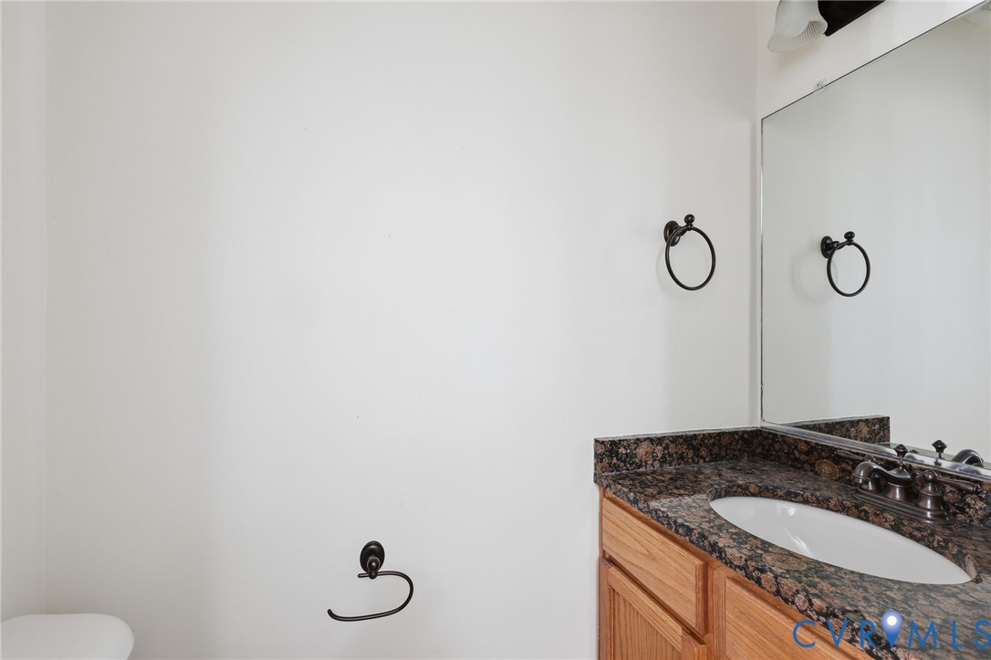 Bathroom vanity featuring a stone-composite countertop, undermount sink, dual-handle faucet, wood cabinetry, and a full-width wall mirror