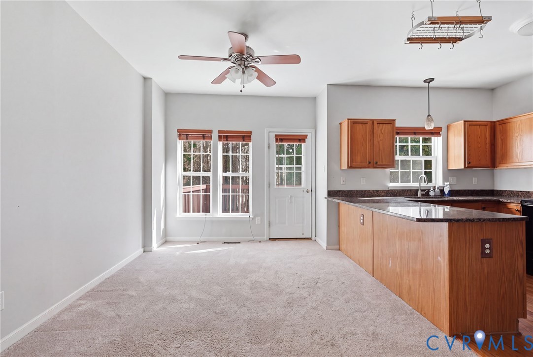 Kitchen featuring wooden cabinetry, dark stone-finish countertops, a breakfast bar, and a ceiling-mounted pot rack, complemented by a ceiling fan with integrated lighting Kitchen featuring wooden cabinetry, dark stone-finish countertops, a breakfast bar, and a ceiling-mounted pot rack, complemented by a ceiling fan with integrated lighting