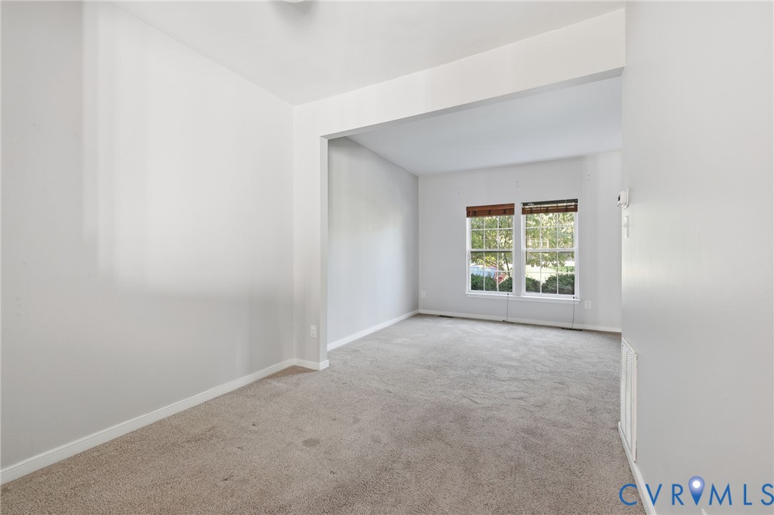Neutral-toned interior featuring wall-to-wall carpeting, wide archway entry, and dual windows with grid-pattern muntins