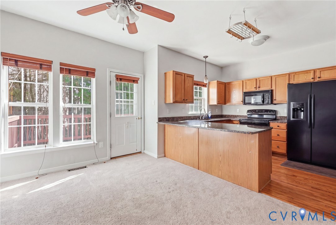 Kitchen featuring light wood cabinetry, stone-finish countertops, black appliances, a ceiling fan, and carpeted flooring