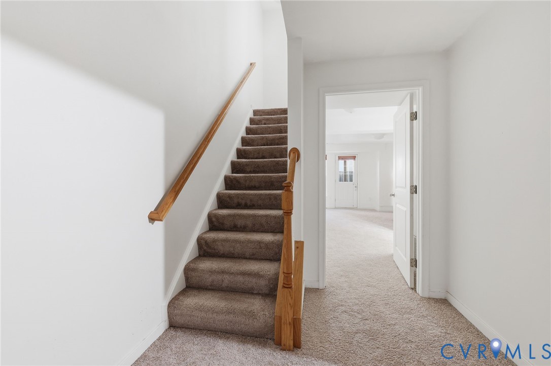 Staircase with carpeted treads, wood-finish handrail, and wooden baluster, featuring neutral-toned carpeting and a multi-panel interior door Staircase with carpeted treads, wood-finish handrail, and wooden baluster, featuring neutral-toned carpeting and a multi-panel interior door
