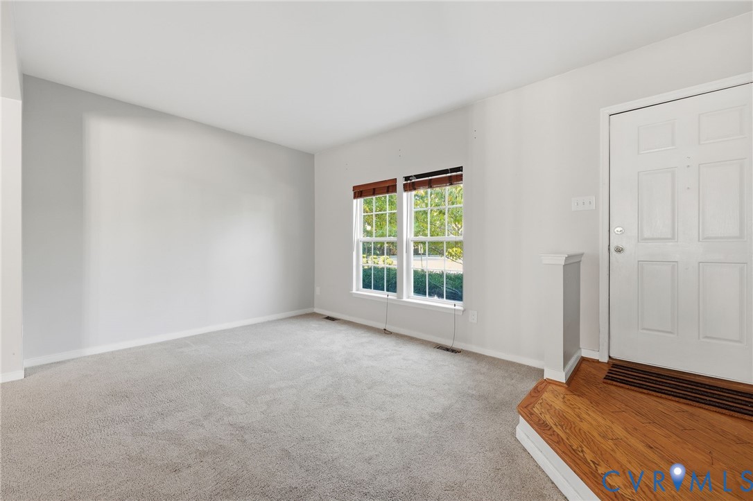Neutral wall palette with plush carpeting, two double-hung windows, and a multi-pane entry door featuring a hardwood-finished platform landing Neutral wall palette with plush carpeting, two double-hung windows, and a multi-pane entry door featuring a hardwood-finished platform landing