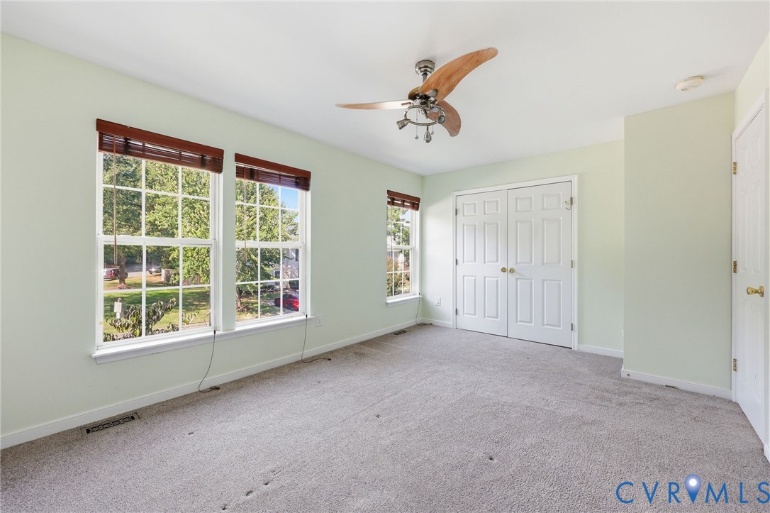 Room featuring wall-to-wall carpeting, dual-pane windows with grid mullions, wooden-finish ceiling fan with integrated lighting, and double-door closet cabinetry
