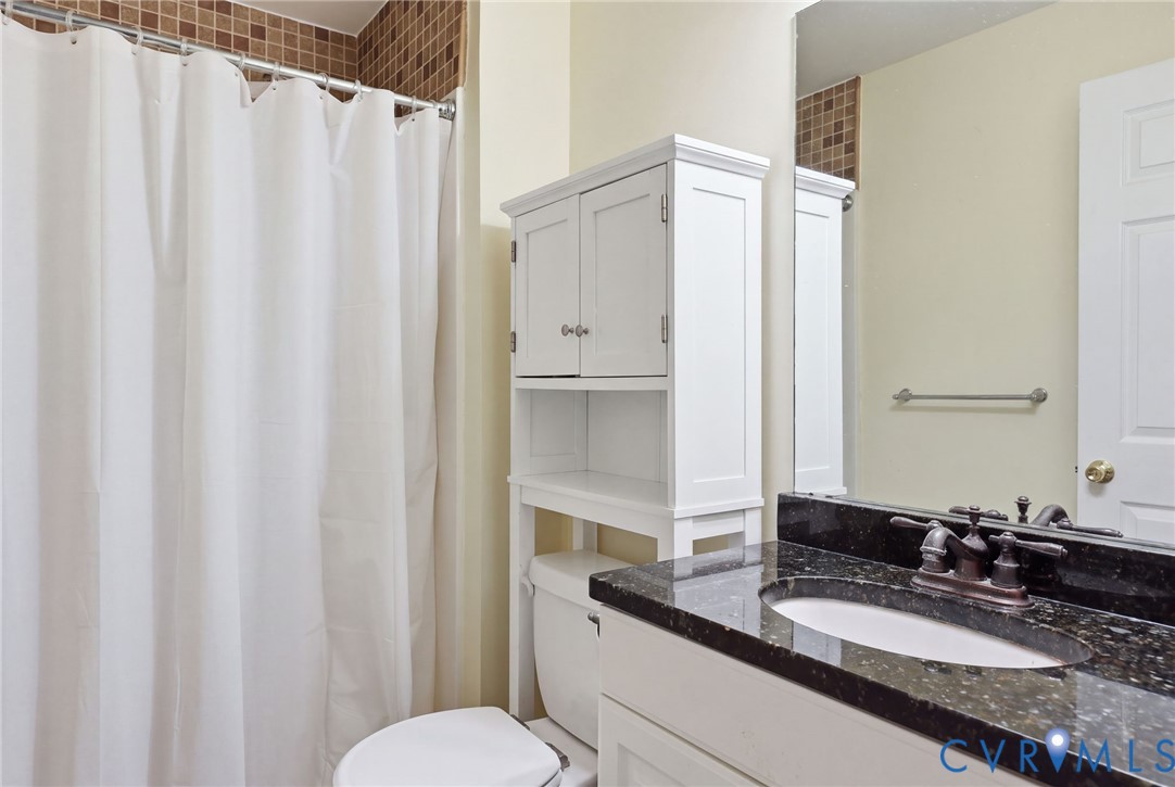 Bathroom featuring a stone-top vanity with an integrated oval sink, dark metal faucet, full-width mirror, and decorative tile accents surrounding the shower area