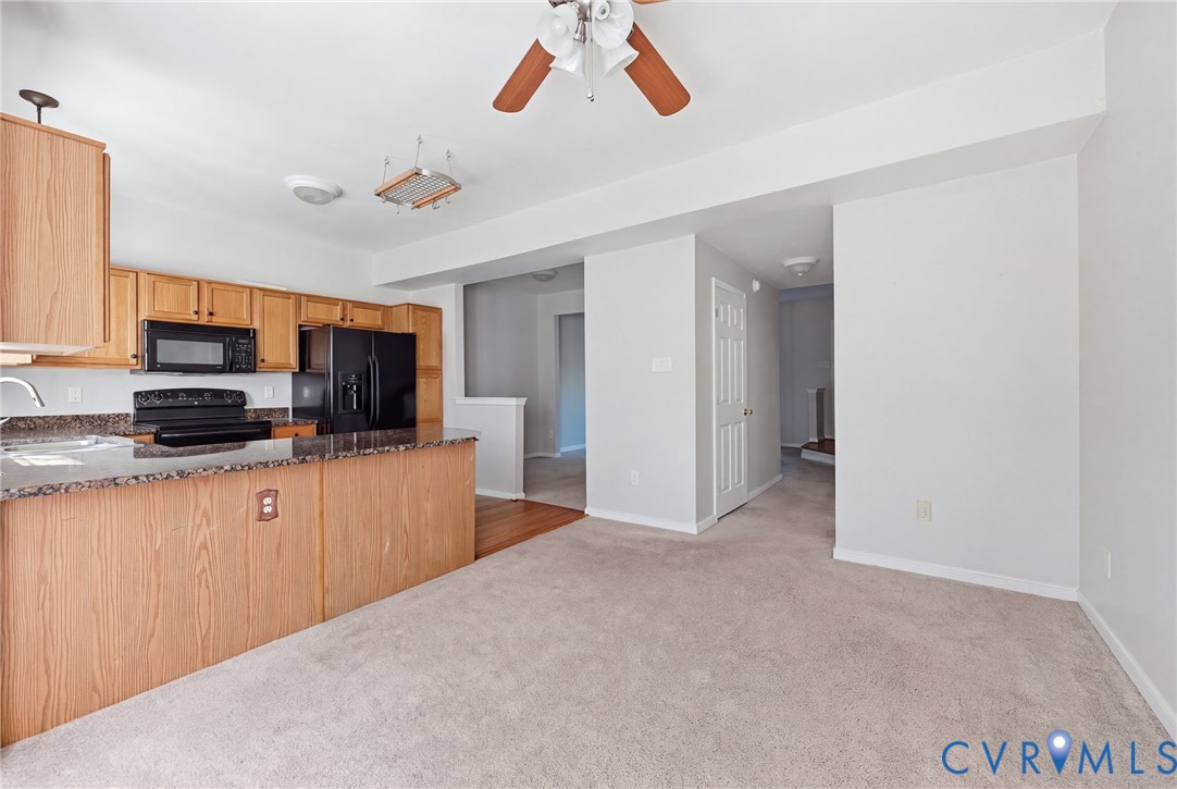 Kitchen featuring wood cabinetry, stone-finish countertops, a black built-in microwave, a black range, and a ceiling fan Kitchen featuring wood cabinetry, stone-finish countertops, a black built-in microwave, a black range, and a ceiling fan