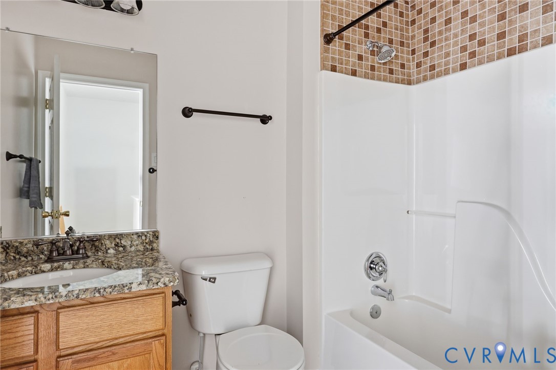Bathroom featuring a vanity with stone-finish countertop, undermount sink, multi-tone mosaic tile shower surround, white composite tub, and dark hardware