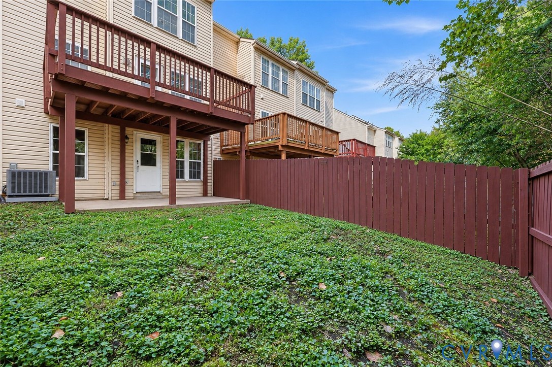 Exterior rear of property featuring a raised wooden deck, ground-level concrete patio, fenced yard, and vinyl siding