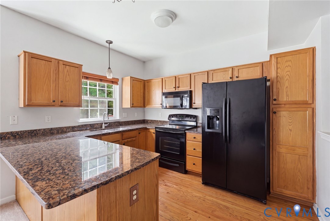 Kitchen featuring wood cabinetry, stone countertops, wood-finish flooring, and black appliances