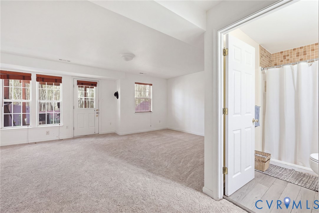 Open floor plan featuring carpeting, multiple windows with grid detailing, a glass-paneled exterior door, and a bathroom with tile flooring and tiled shower enclosure