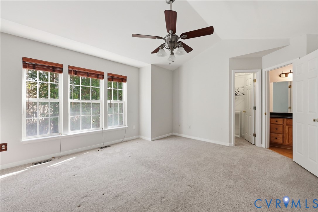 Vaulted ceiling featuring a central multi-blade ceiling fan, wall-to-wall carpeting, and a triple-window configuration with integrated wooden blinds