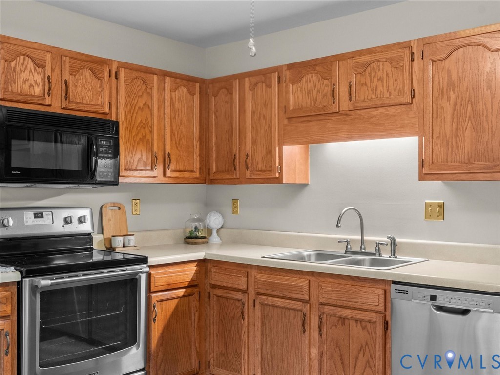 Kitchen featuring raised-panel oak cabinetry, stainless steel appliances, dual-basin stainless steel sink, and solid-surface countertops Kitchen featuring raised-panel oak cabinetry, stainless steel appliances, dual-basin stainless steel sink, and solid-surface countertops