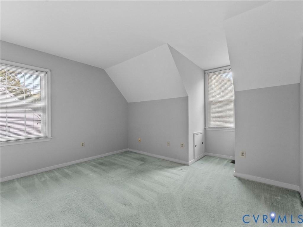 Neutral-toned room featuring angled ceilings, wall-to-wall carpeting, two double-hung windows, and a built-in knee-wall access door