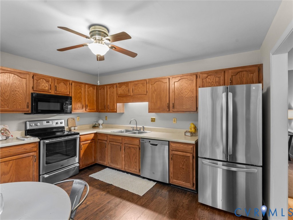 Kitchen featuring stained wood cabinetry, stainless steel appliances, solid surface countertops, dual-basin sink, and wood-finish flooring Kitchen featuring stained wood cabinetry, stainless steel appliances, solid surface countertops, dual-basin sink, and wood-finish flooring