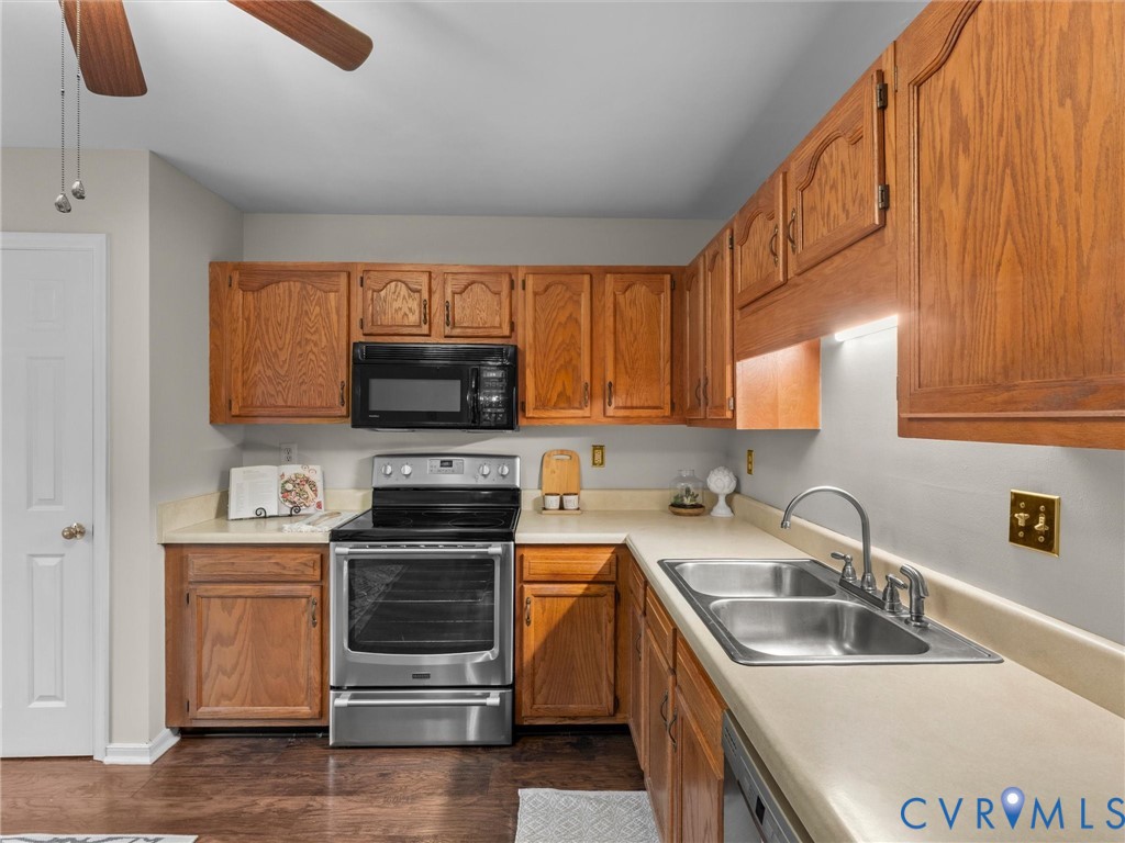Kitchen featuring wood cabinetry, stainless steel appliances, solid-surface countertops, dual-basin stainless steel sink, and wood-finish flooring Kitchen featuring wood cabinetry, stainless steel appliances, solid-surface countertops, dual-basin stainless steel sink, and wood-finish flooring