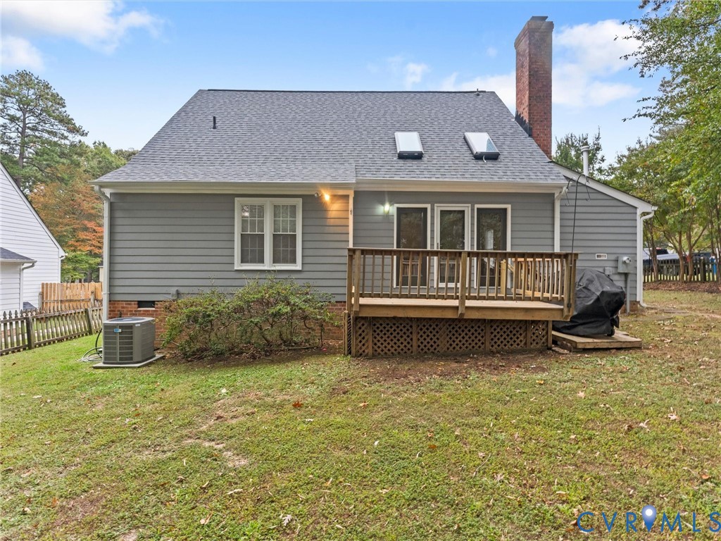 Rear exterior featuring gray horizontal siding, a brick chimney, two roof skylights, and a wood deck with lattice skirting