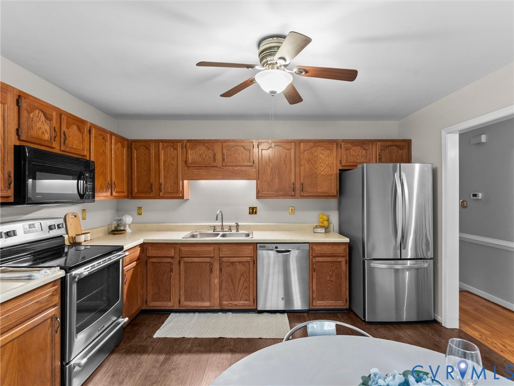 Kitchen featuring wood cabinetry, stainless steel appliances, dual-basin sink, and wood-finish flooring Kitchen featuring wood cabinetry, stainless steel appliances, dual-basin sink, and wood-finish flooring