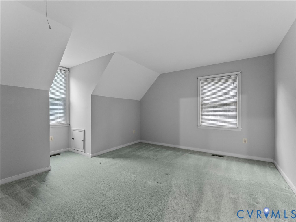 Room featuring neutral wall tones, carpet flooring, vaulted ceilings, and two windows