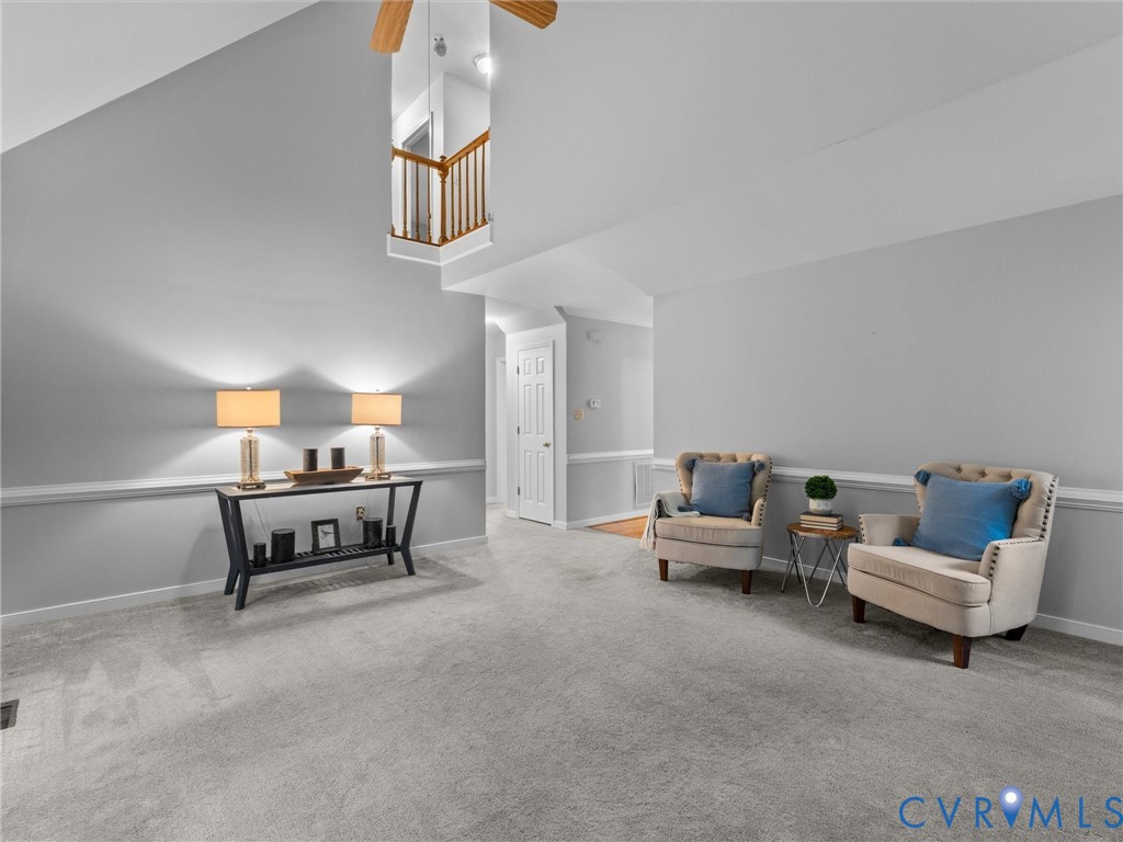 Vaulted ceiling, carpeted flooring, chair rail molding, and a mezzanine balcony featuring a wooden railing