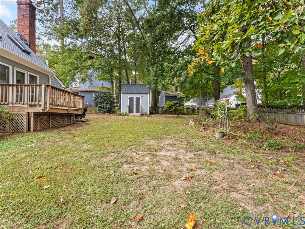 Backyard featuring a raised wooden deck with lattice skirting, an exterior storage shed, mature trees, and wooden perimeter fencing