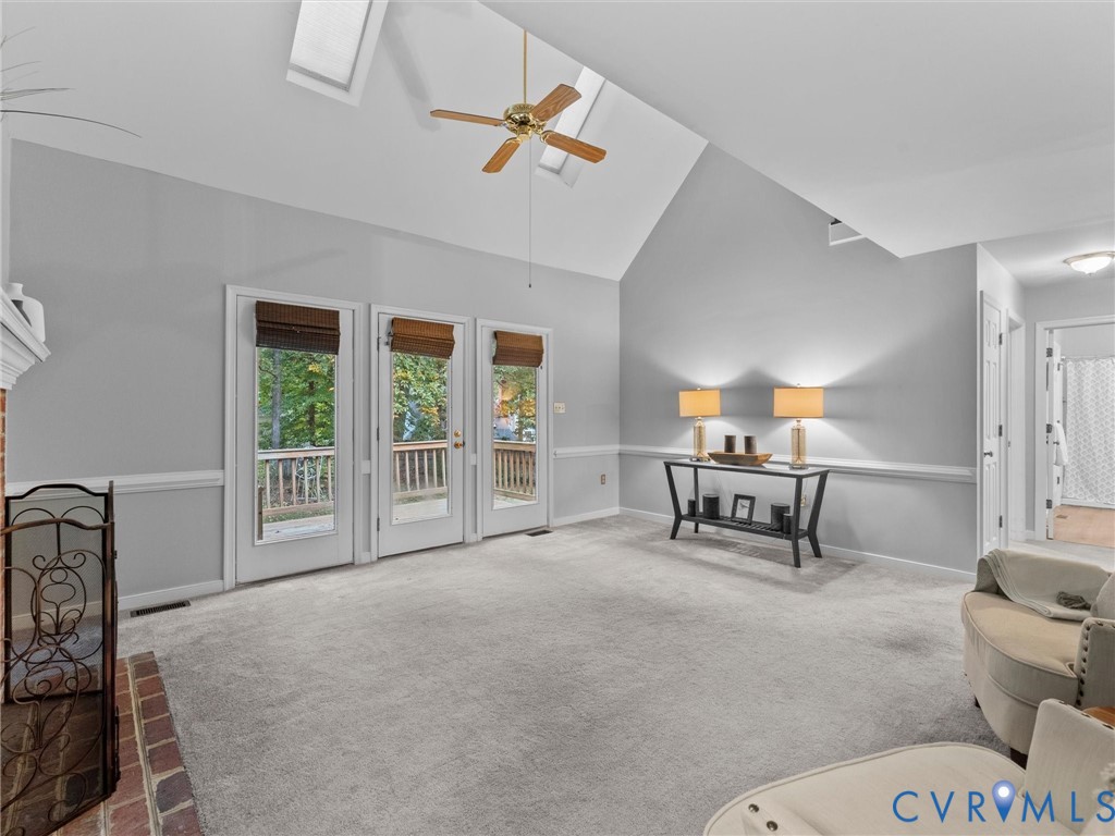 Vaulted ceiling with dual skylights, brick hearth fireplace, and three glass-paneled exterior doors leading to a wood-railed deck