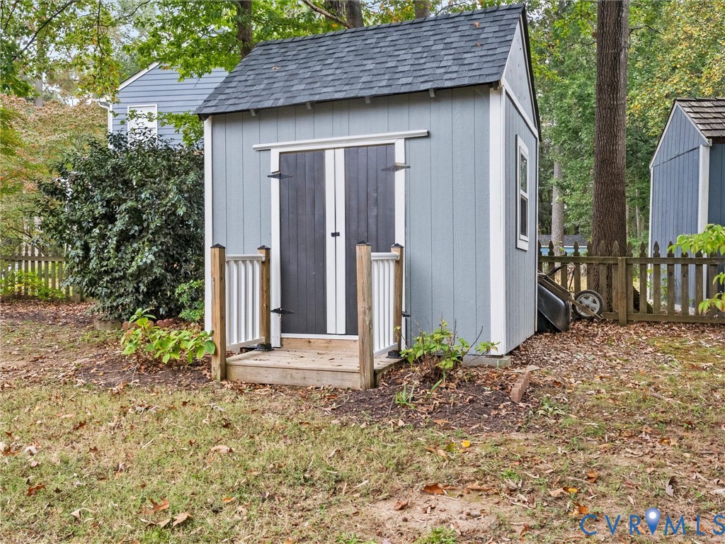 Storage shed featuring shingle roofing, double doors, and an elevated entryway with white railing