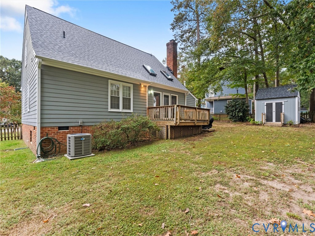 Rear exterior featuring horizontal lap siding, brick foundation, raised wooden deck, roof skylights, and a detached storage structure