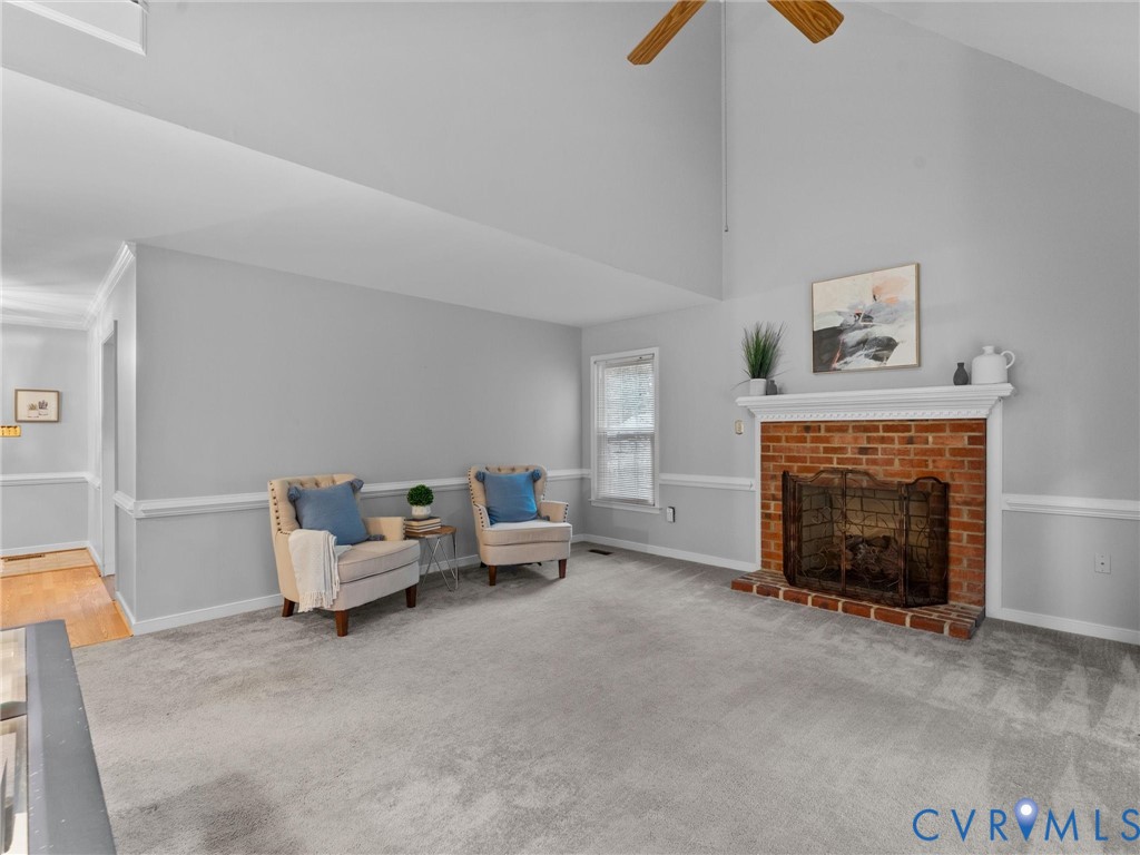 Vaulted ceiling featuring a central wooden ceiling fan, brick fireplace with a white mantel, and chair rail molding