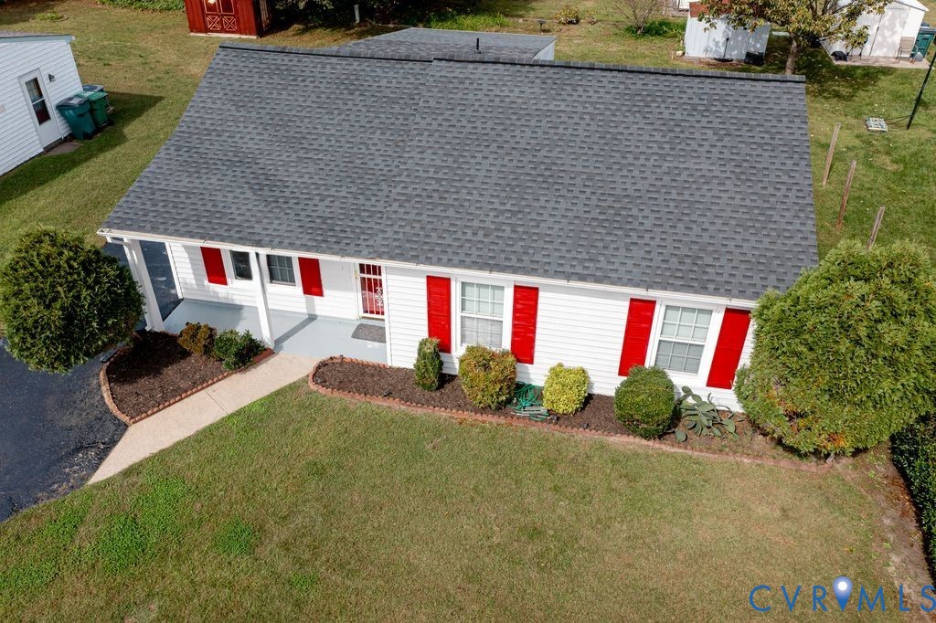 Ranch-style residence featuring white siding, red window shutters, a dark shingle roof, a covered front porch with concrete flooring, and a landscaped front garden bed with a stone border Ranch-style residence featuring white siding, red window shutters, a dark shingle roof, a covered front porch with concrete flooring, and a landscaped front garden bed with a stone border
