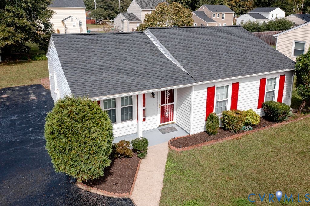 Single-story residence featuring white siding, red window shutters, asphalt shingle roof, paved driveway, and landscaped garden beds with stone edging Single-story residence featuring white siding, red window shutters, asphalt shingle roof, paved driveway, and landscaped garden beds with stone edging
