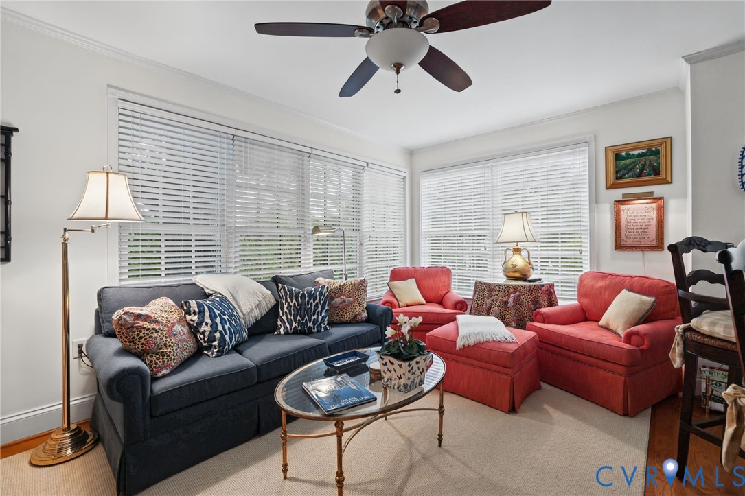 Living area featuring multi-pane windows, hardwood flooring, and a ceiling fan with integrated lighting