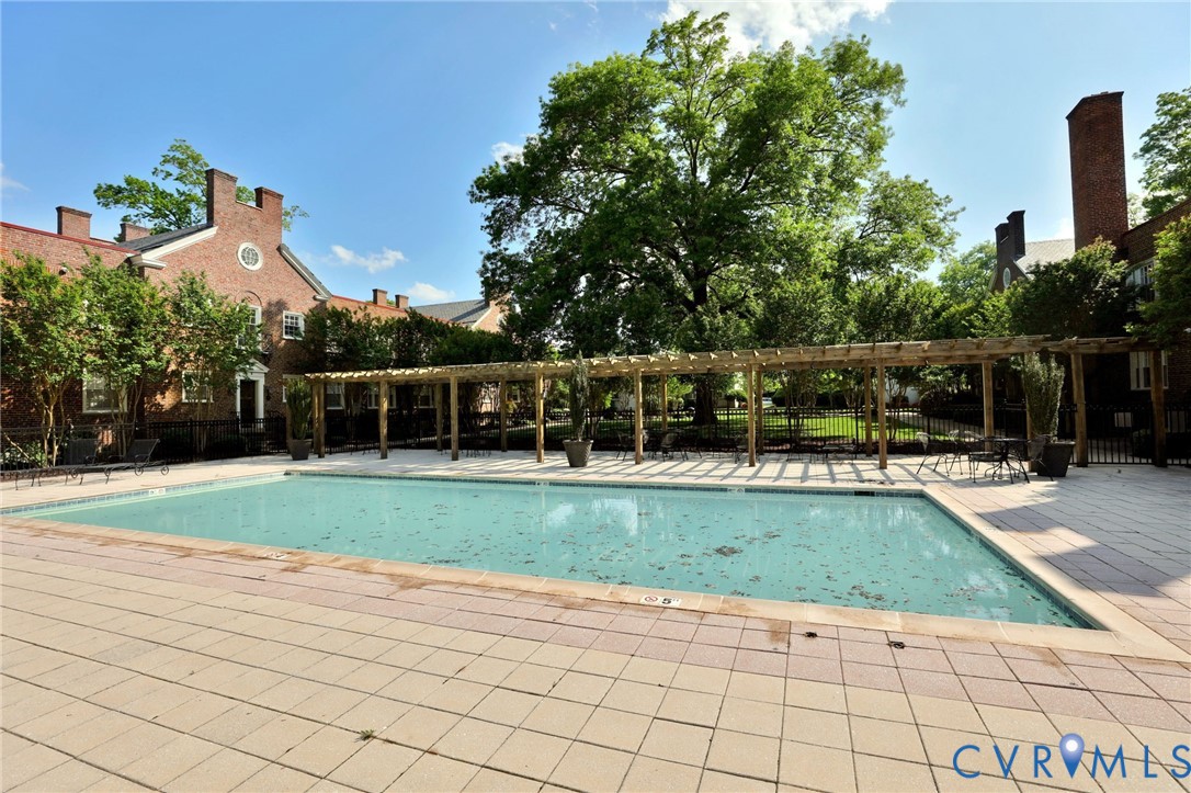 In-ground swimming pool featuring a tile surround, perimeter wood pergola, brick exterior architecture, and mature landscaping