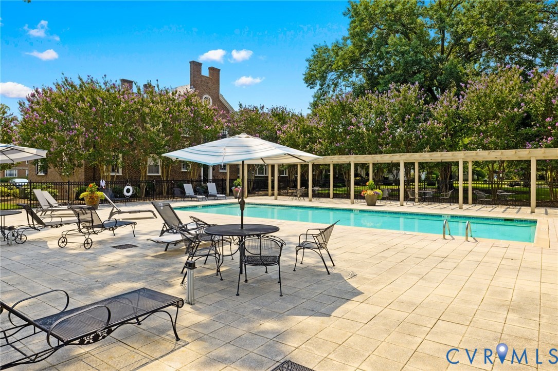 Rectangular swimming pool featuring a concrete paver deck, metal pergola, and perimeter metal fencing