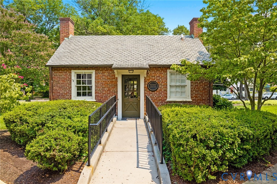 Brick exterior featuring two chimneys, multi-pane windows with shutters, concrete entryway ramp with metal railings, and mature landscaping