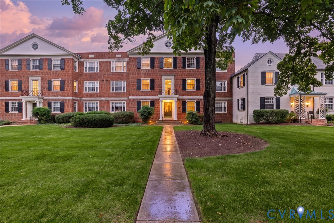 Colonial architecture featuring a brick facade, shuttered multi-pane windows, decorative pediments, and a central paved walkway Colonial architecture featuring a brick facade, shuttered multi-pane windows, decorative pediments, and a central paved walkway