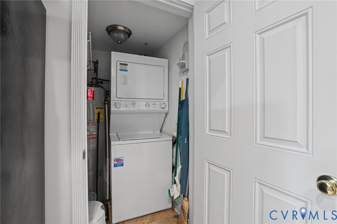 Utility closet featuring a stacked washer and dryer unit, integrated water heater, ceiling-mounted light fixture, and paneled door