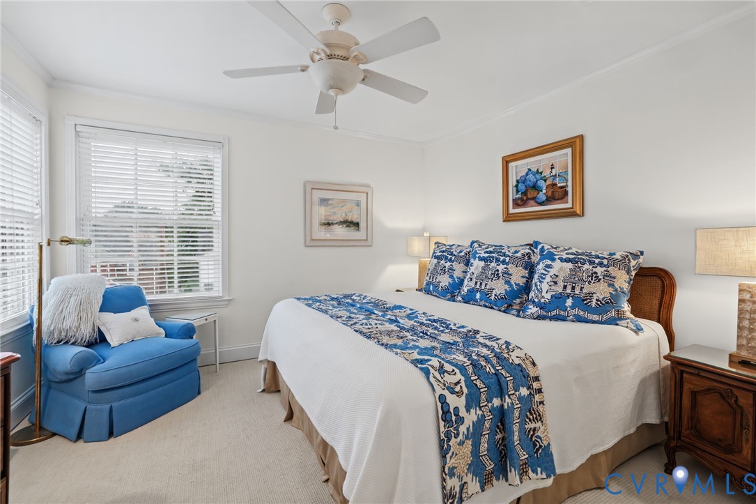 Bedroom featuring neutral carpet, white walls, dual windows with white horizontal blinds, and a white ceiling fan with integrated lighting
