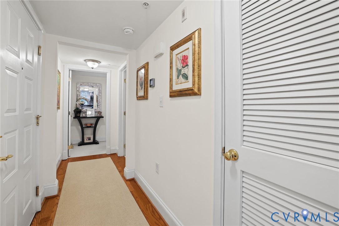 Interior hallway featuring wood-finish flooring, white paneled doors, and louvered closet doors with polished brass hardware