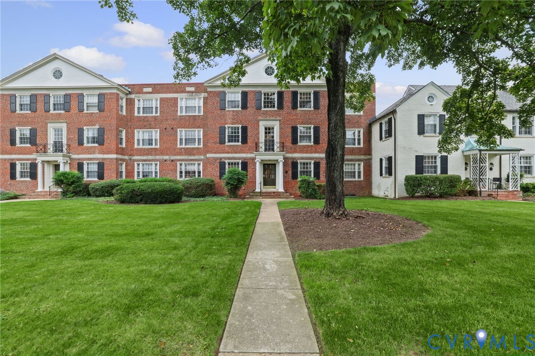 Georgian-inspired brick exterior featuring a multi-story facade, decorative shutters, pedimented entryways, a manicured lawn, and mature trees