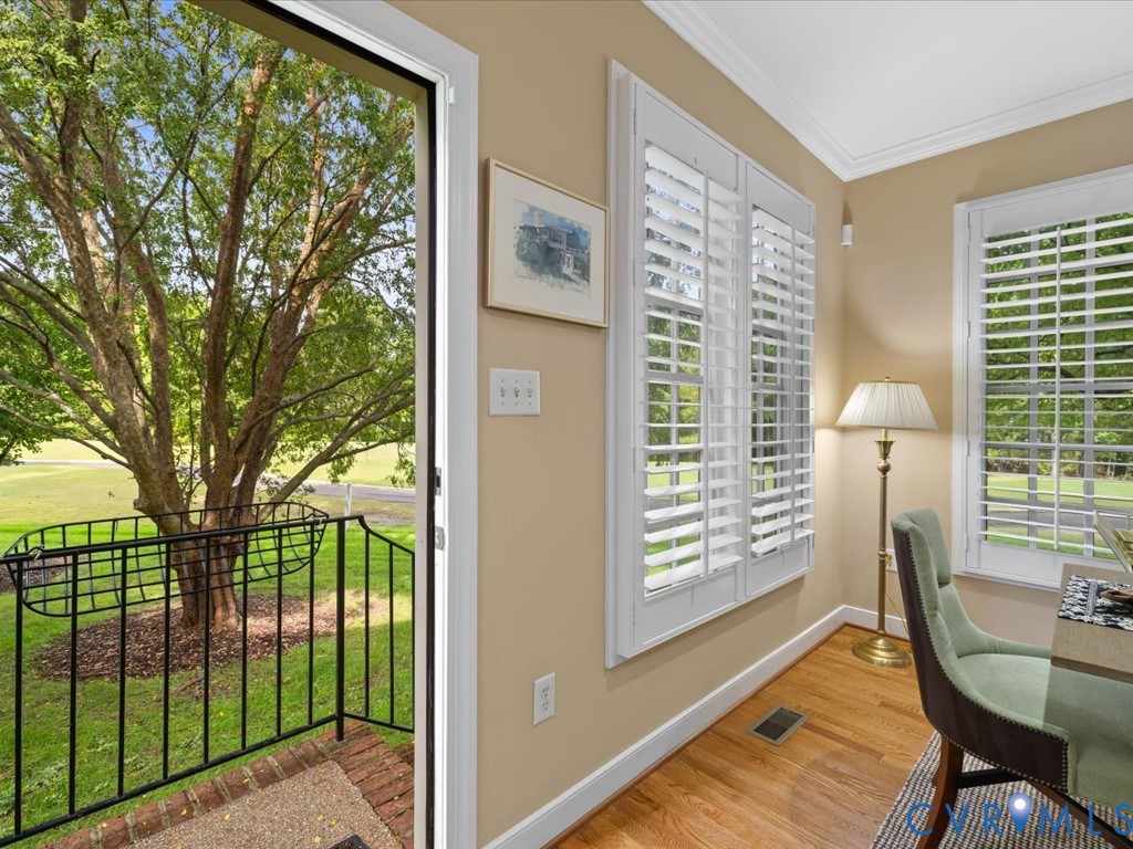 Wood-finish flooring, white plantation shutters, crown molding, and a brick-finish entryway