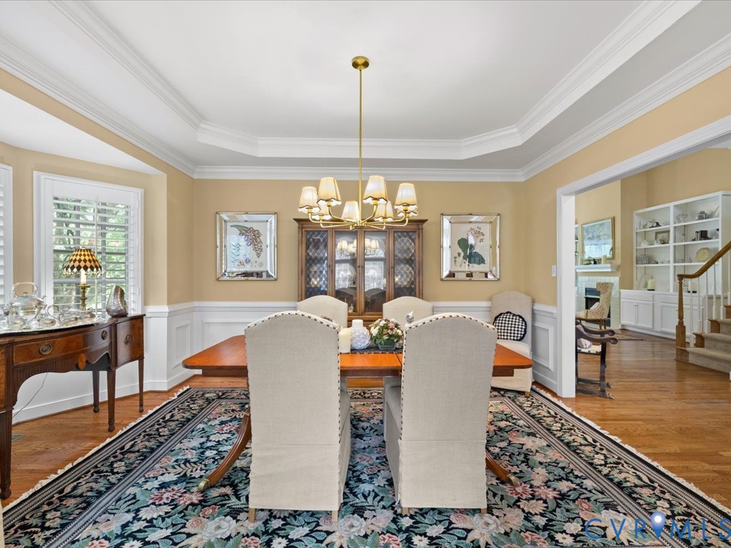 Tray ceiling with crown molding, wood-finish flooring, white wainscoting, and large windows with plantation shutters