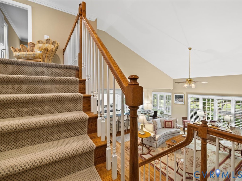 Carpeted staircase with wood handrail, open concept living area, vaulted ceiling, and ample natural light through multiple windows
