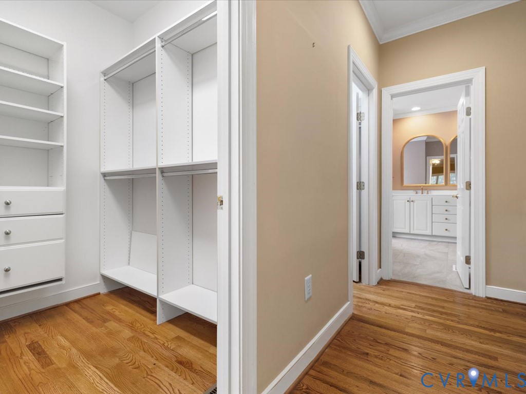 Hardwood flooring, custom closet shelving, built-in closet drawers, arched mirrors, and white vanity cabinetry